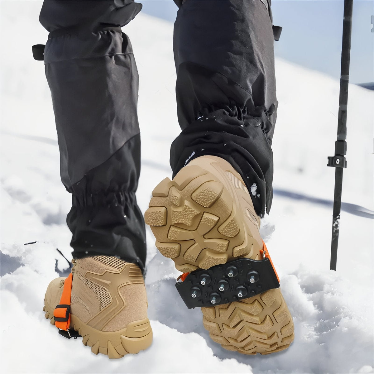 Walker in snow with an ice cleat strapped under the arch of a tan boot, trekking pole beside