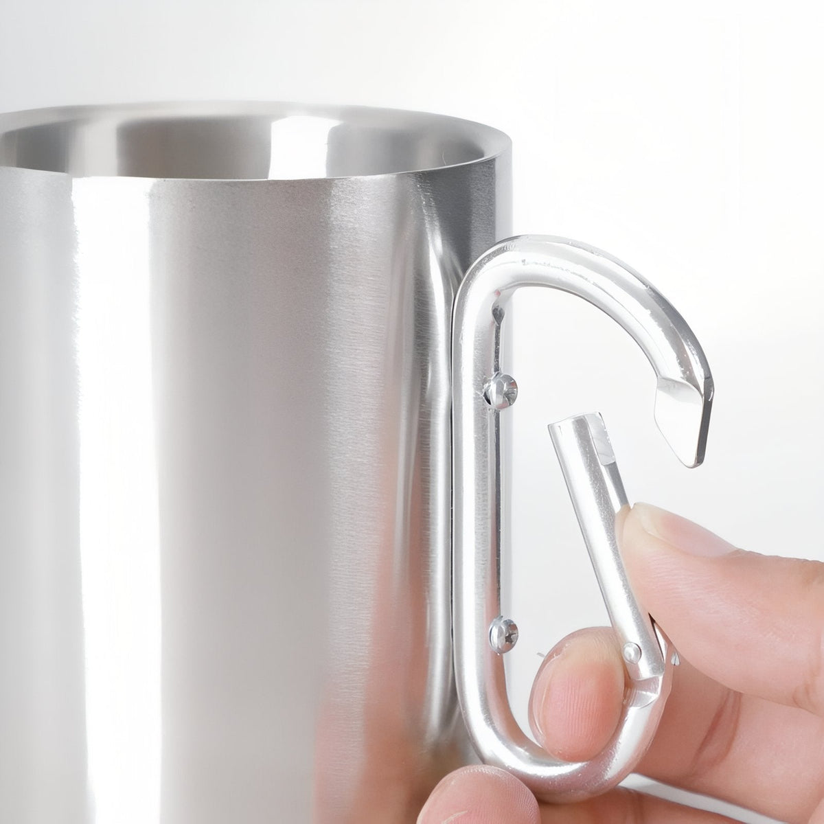 Fingers pressing open the spring gate of the mug's carabiner handle