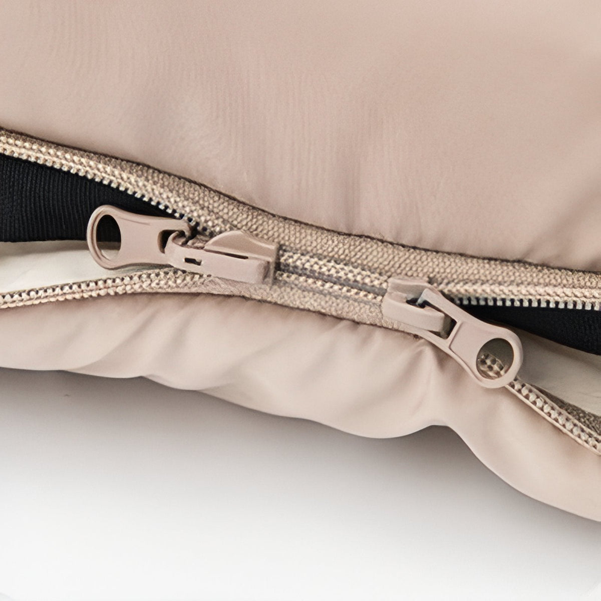 Close-up of the side zip of the sleeping bag with two beige zip sliders and the cream lining inside