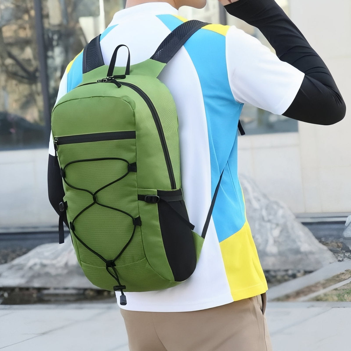 Person seen from behind wearing a green packable daypack with a black bungee cord on the front
