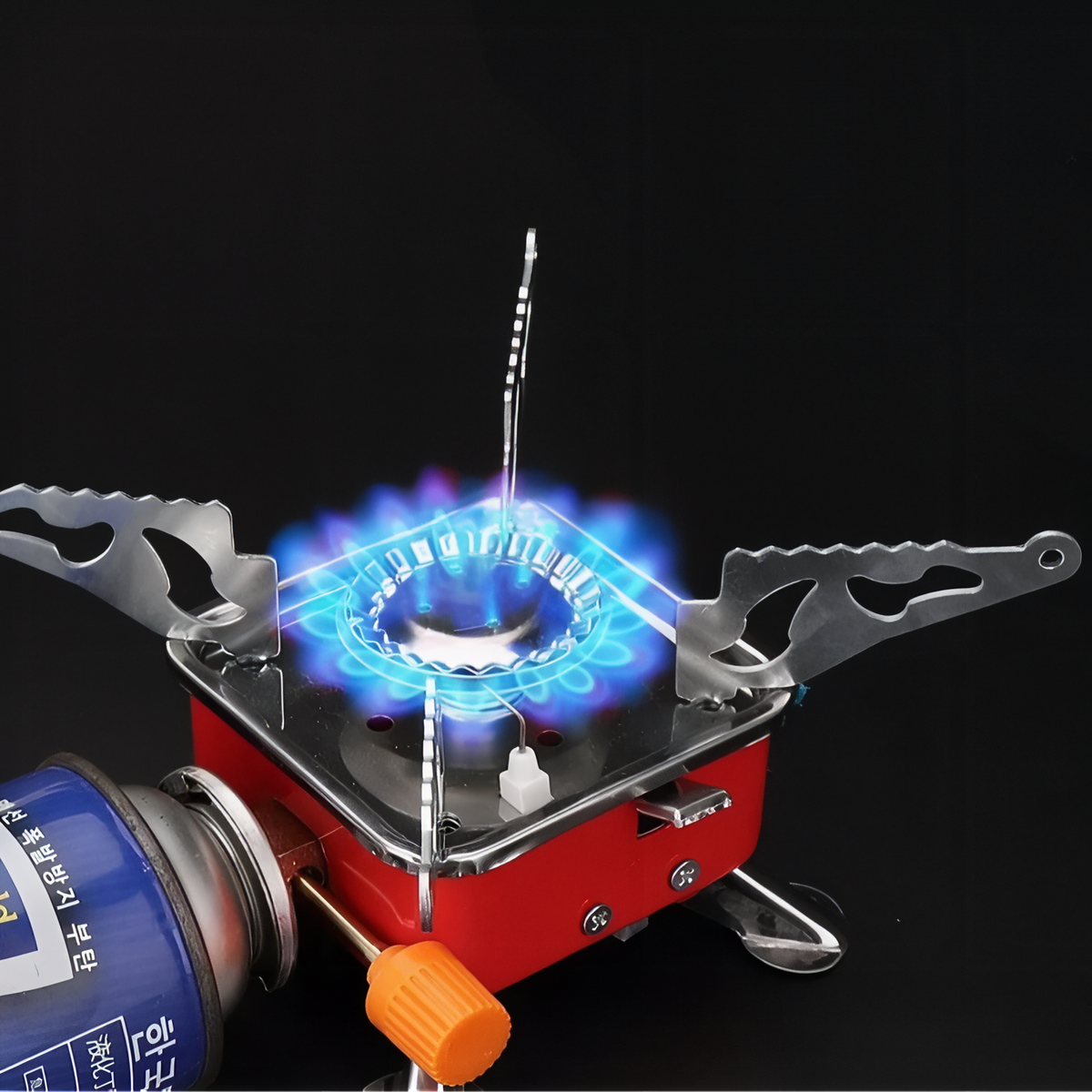 Red camping stove lit with a ring of blue flame, a gas cartridge connected at the side