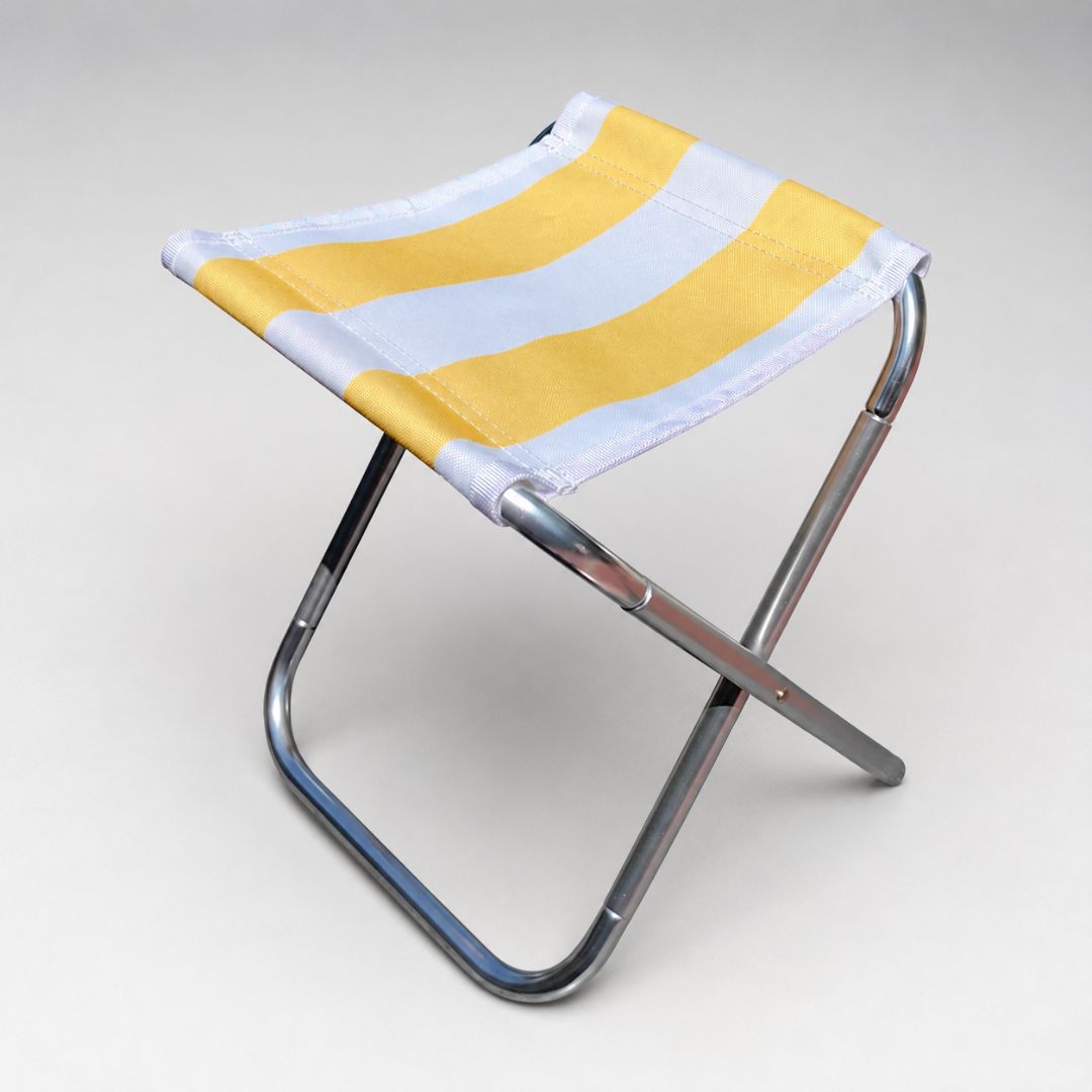 A folding stool with a slim silver frame and a yellow and white striped seat, seen from above on a pale grey background.