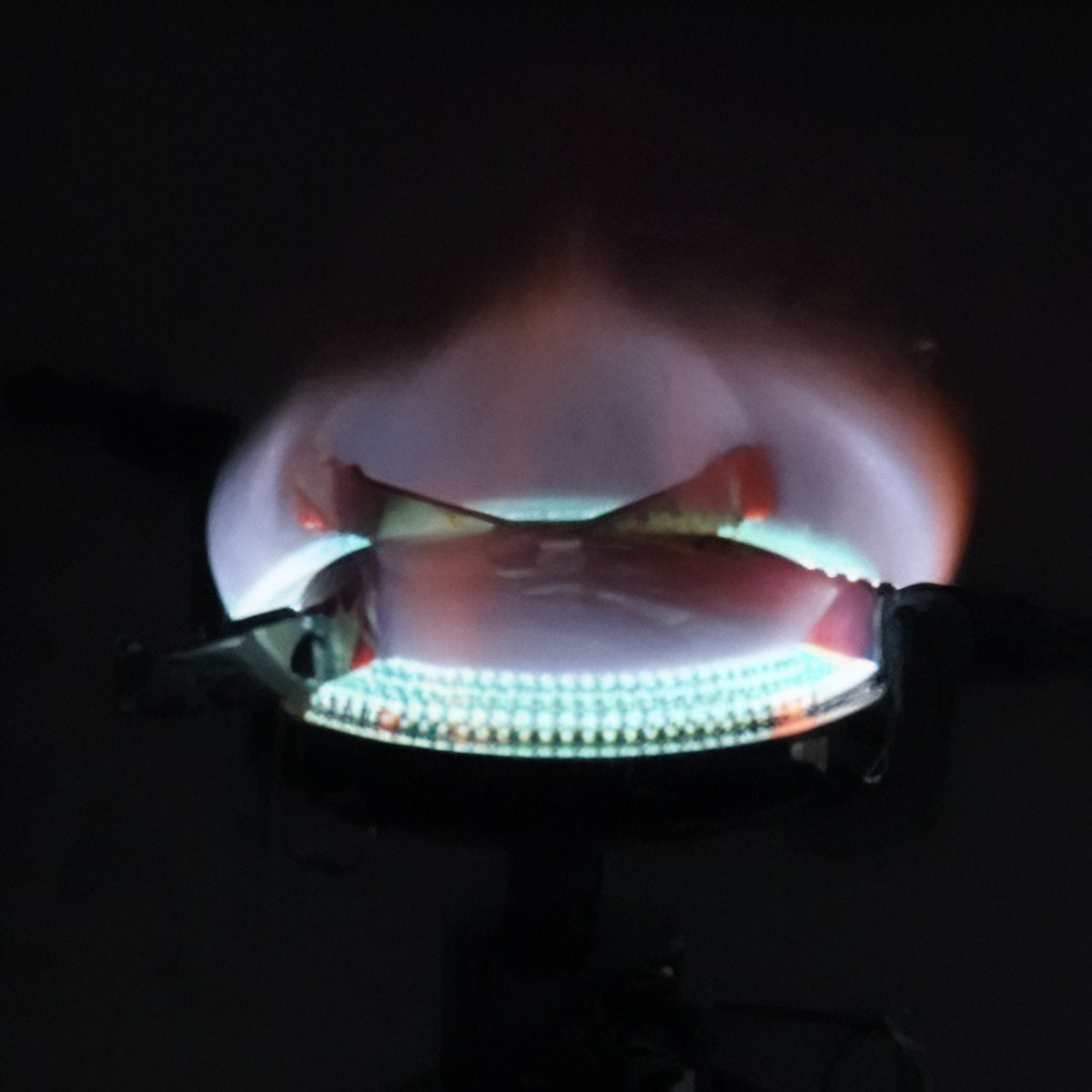 Blue gas flame burning round the stove's wind-shielded burner in the dark