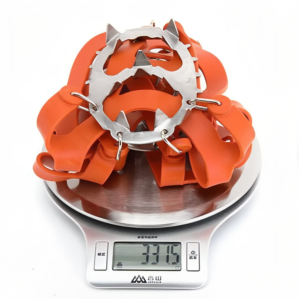 Folded pair of orange crampons on a kitchen scale reading about 331 g