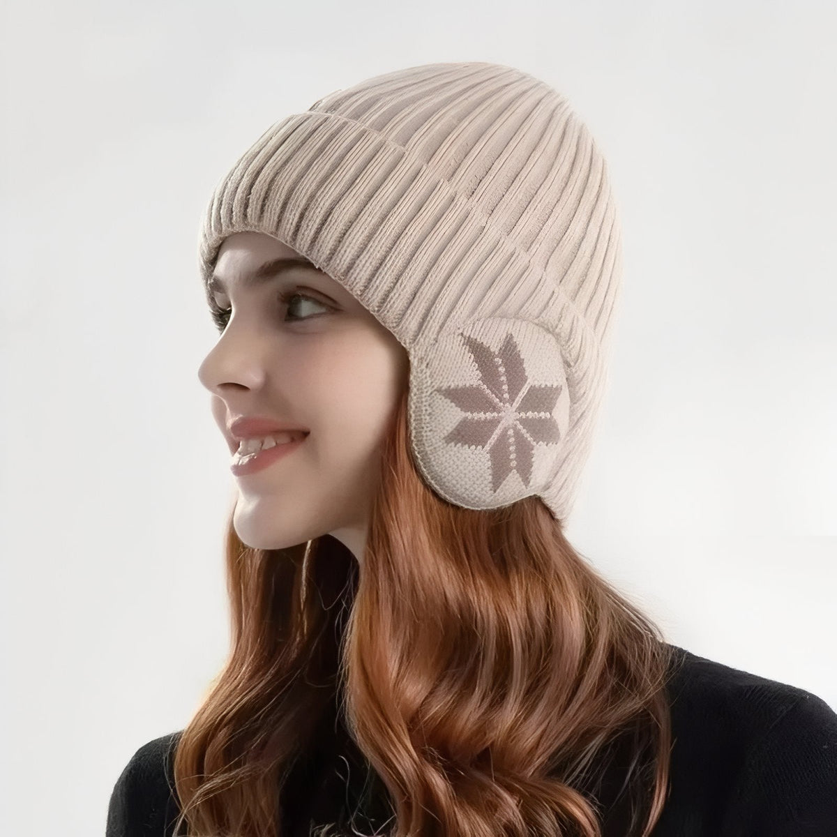 Woman wearing the light beige knit beanie with its snowflake ear flaps over her ears, side view