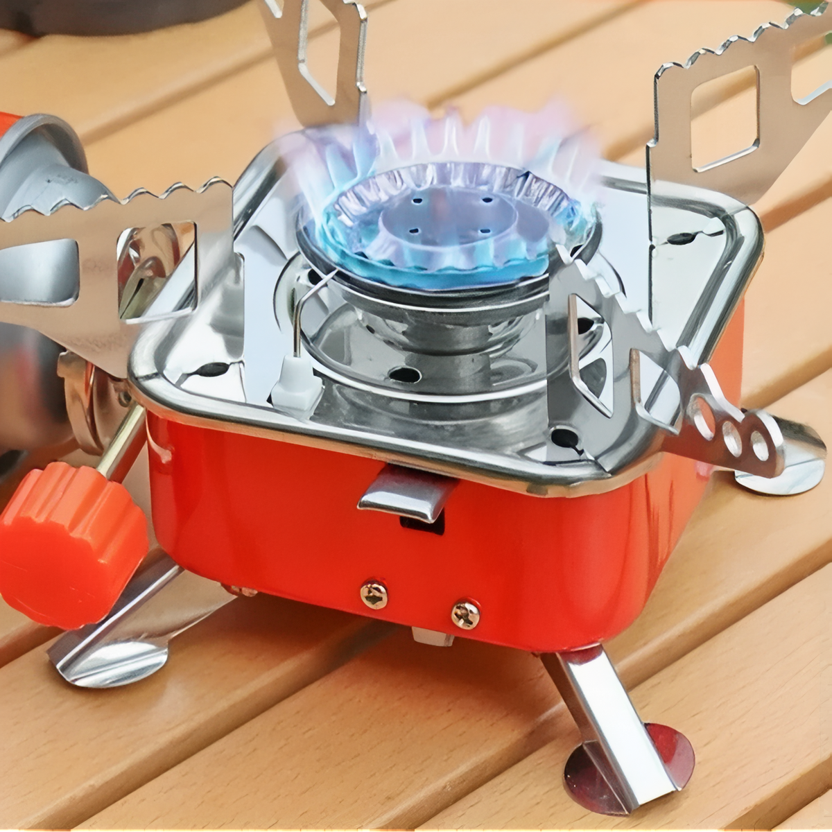Red camping stove lit with a blue flame on a wooden table, orange valve knob in front