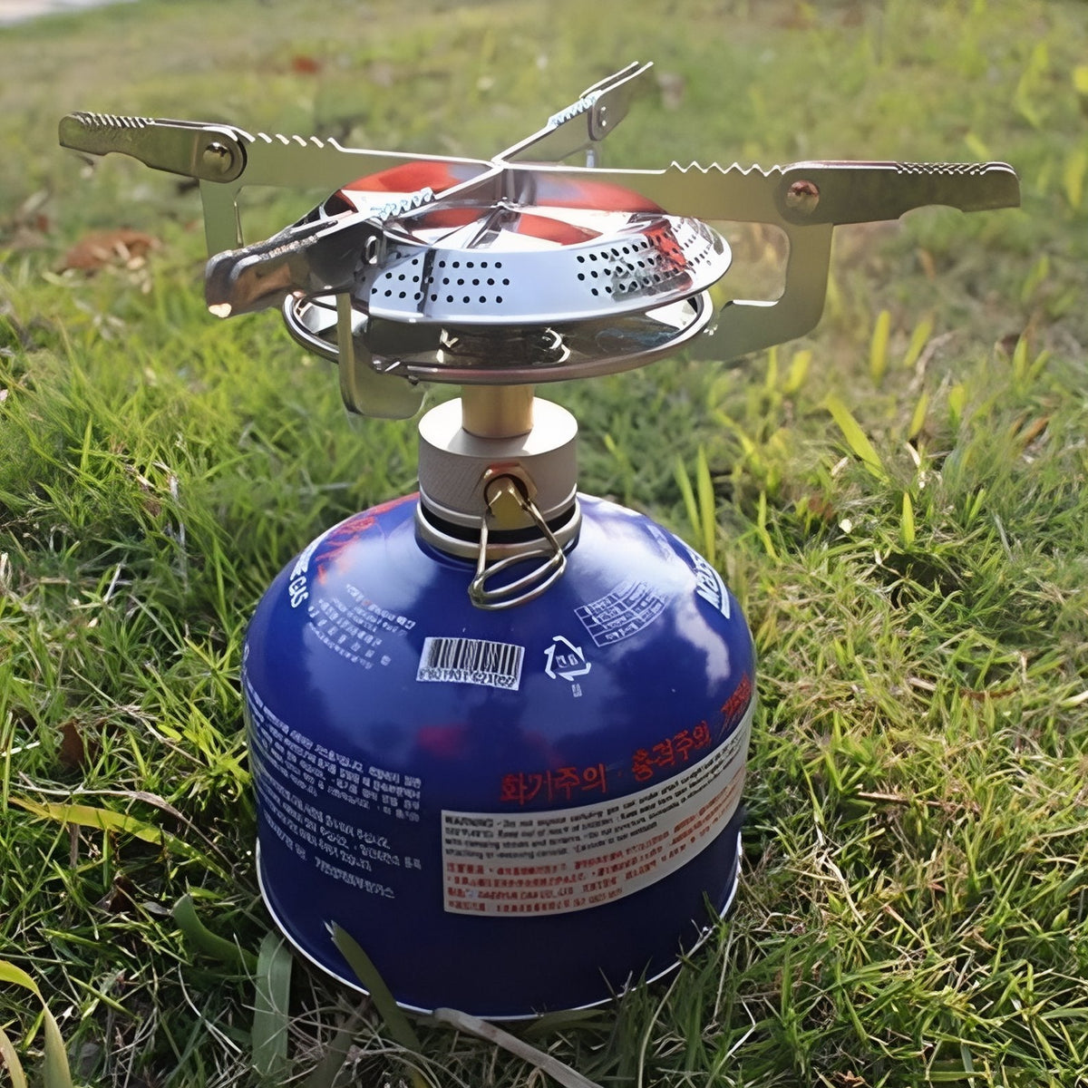 Camping stove on a gas canister standing on grass, pot supports open