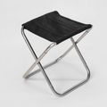 A folding stool with a brushed silver-grey frame and a plain black canvas seat, standing on a light grey background.
