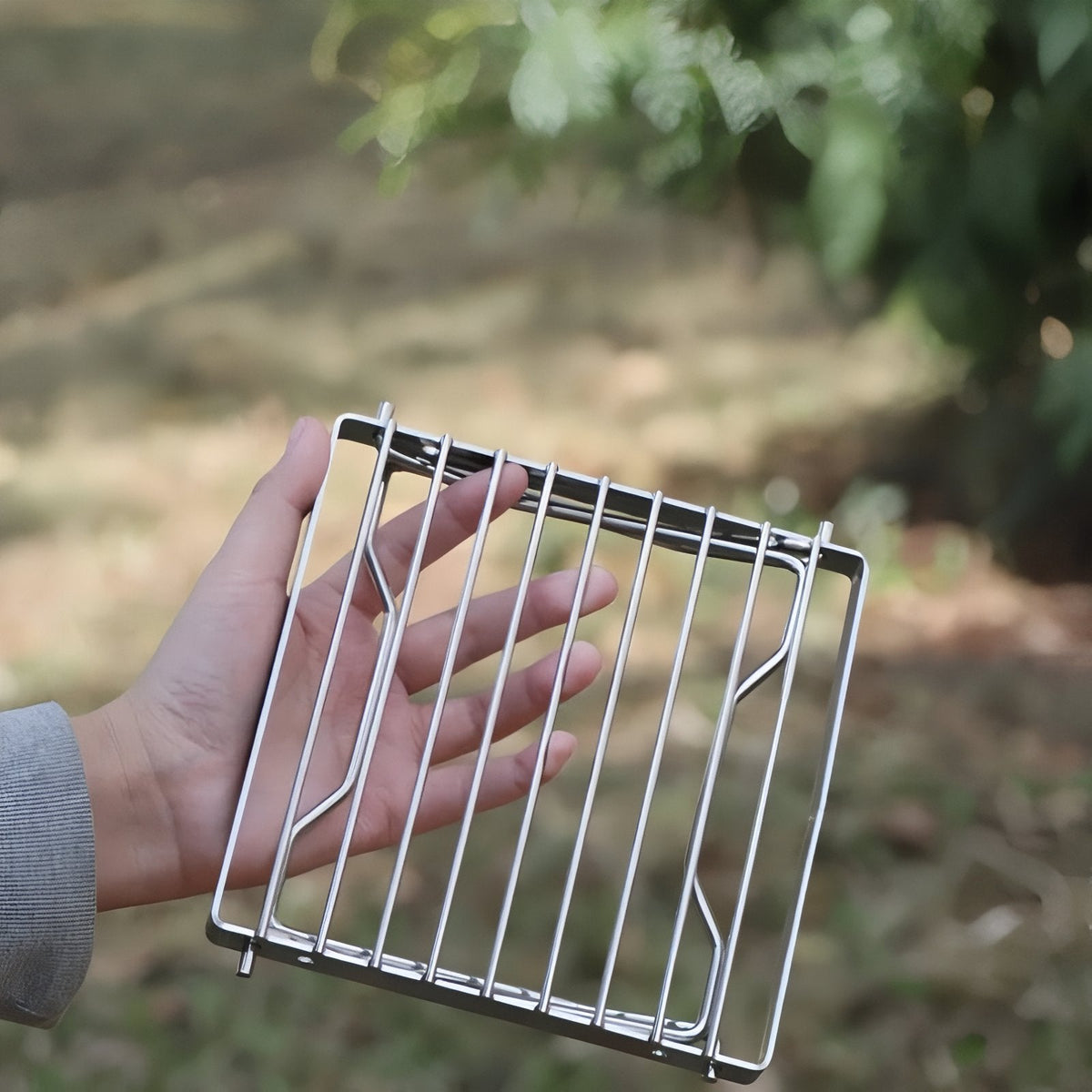 The grill stand folded flat and held in one hand