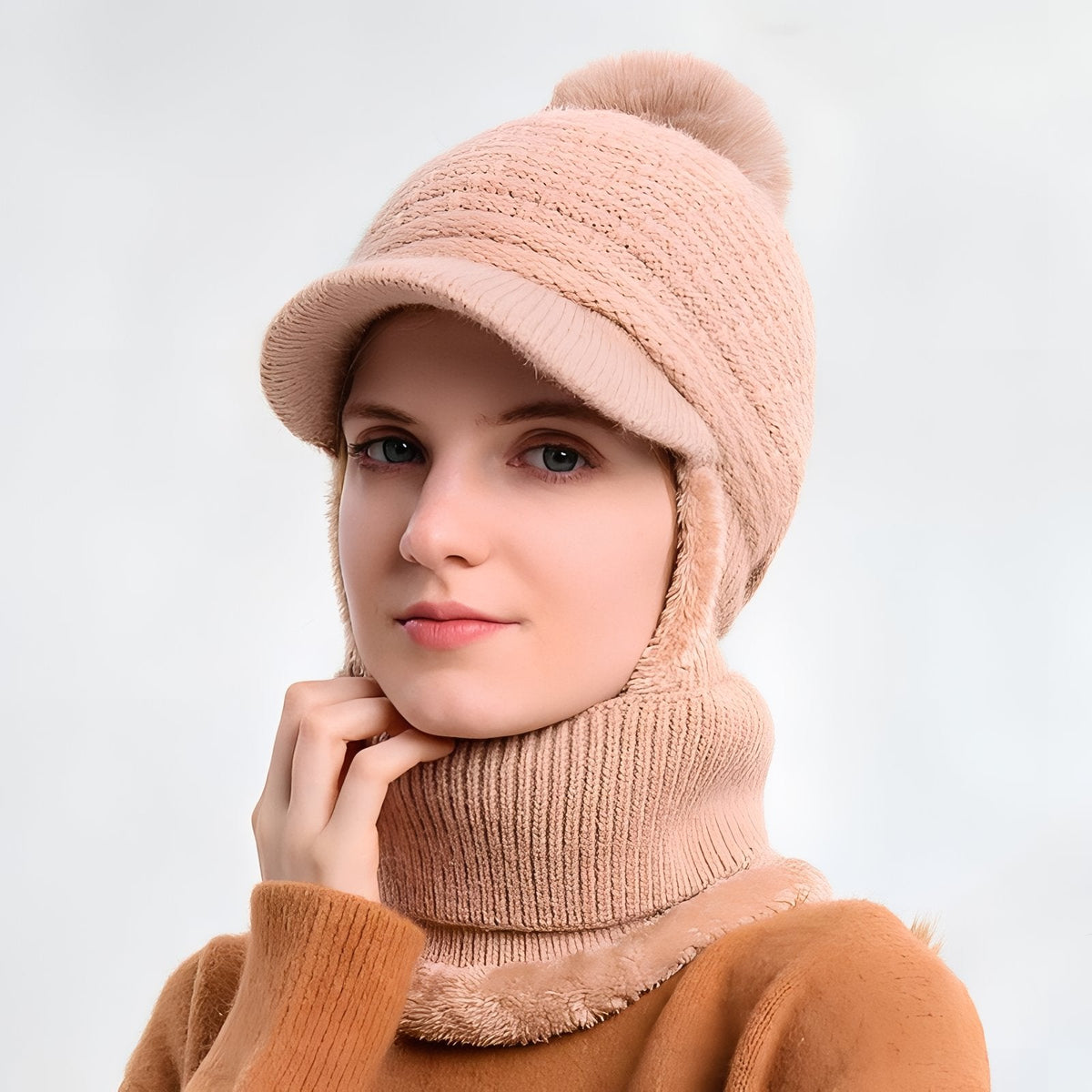 Woman wearing the pink knitted brim beanie with pompom, ear flaps down and the neck warmer round her throat