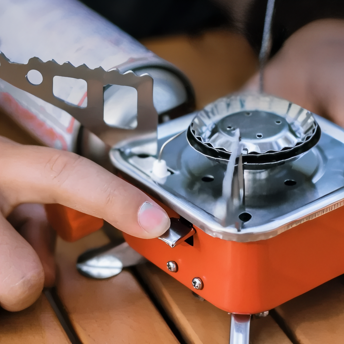 Hand pressing the piezo lever of the red stove, a gas cartridge connected at the side