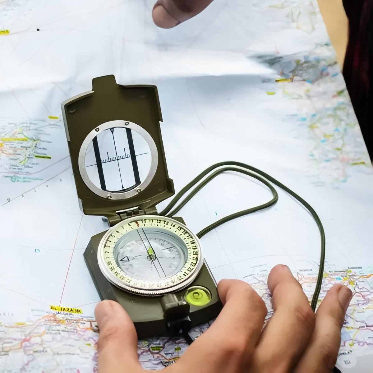 Hands taking a bearing with the open olive green lensatic compass on a paper map