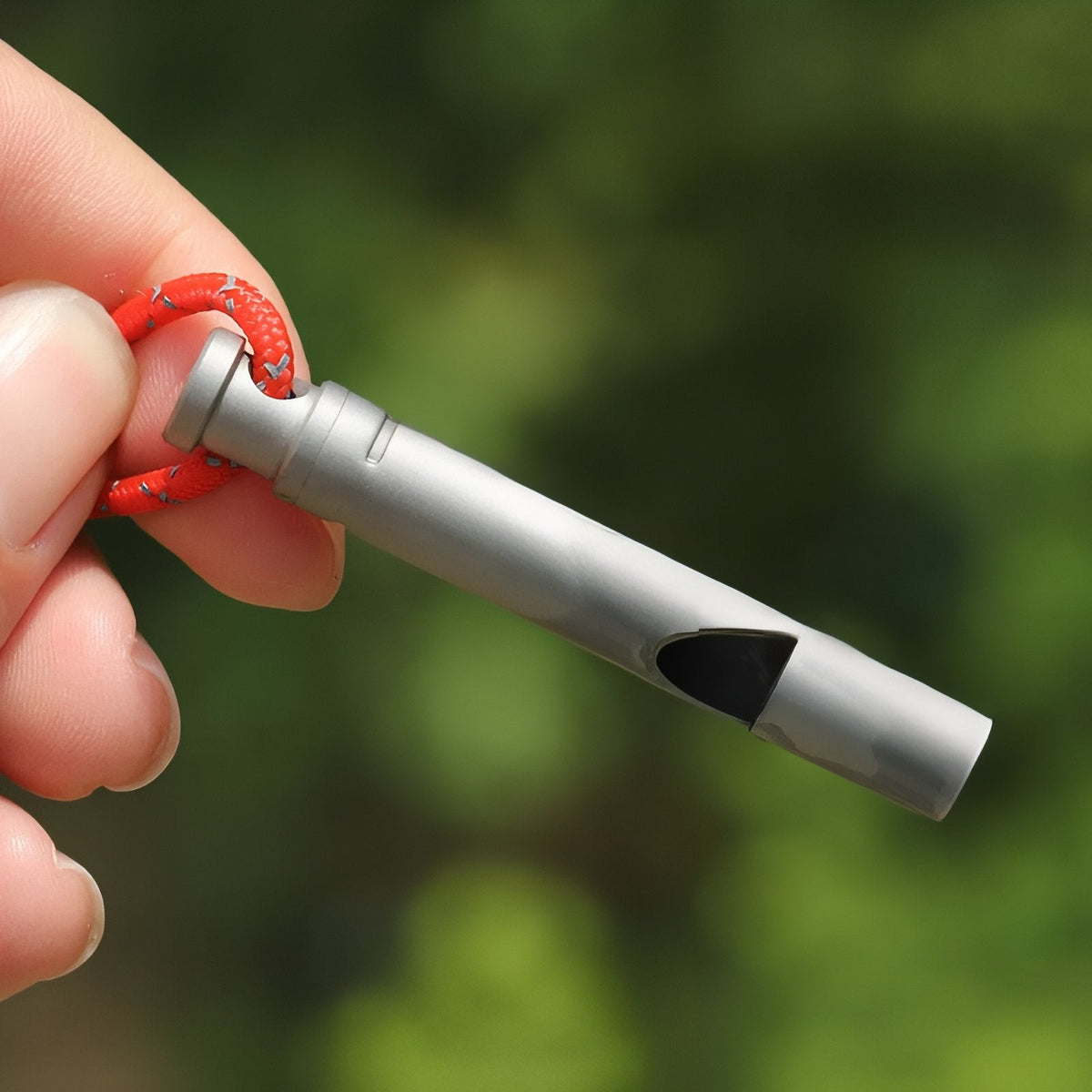 Fingers holding the titanium whistle by its red cord outdoors