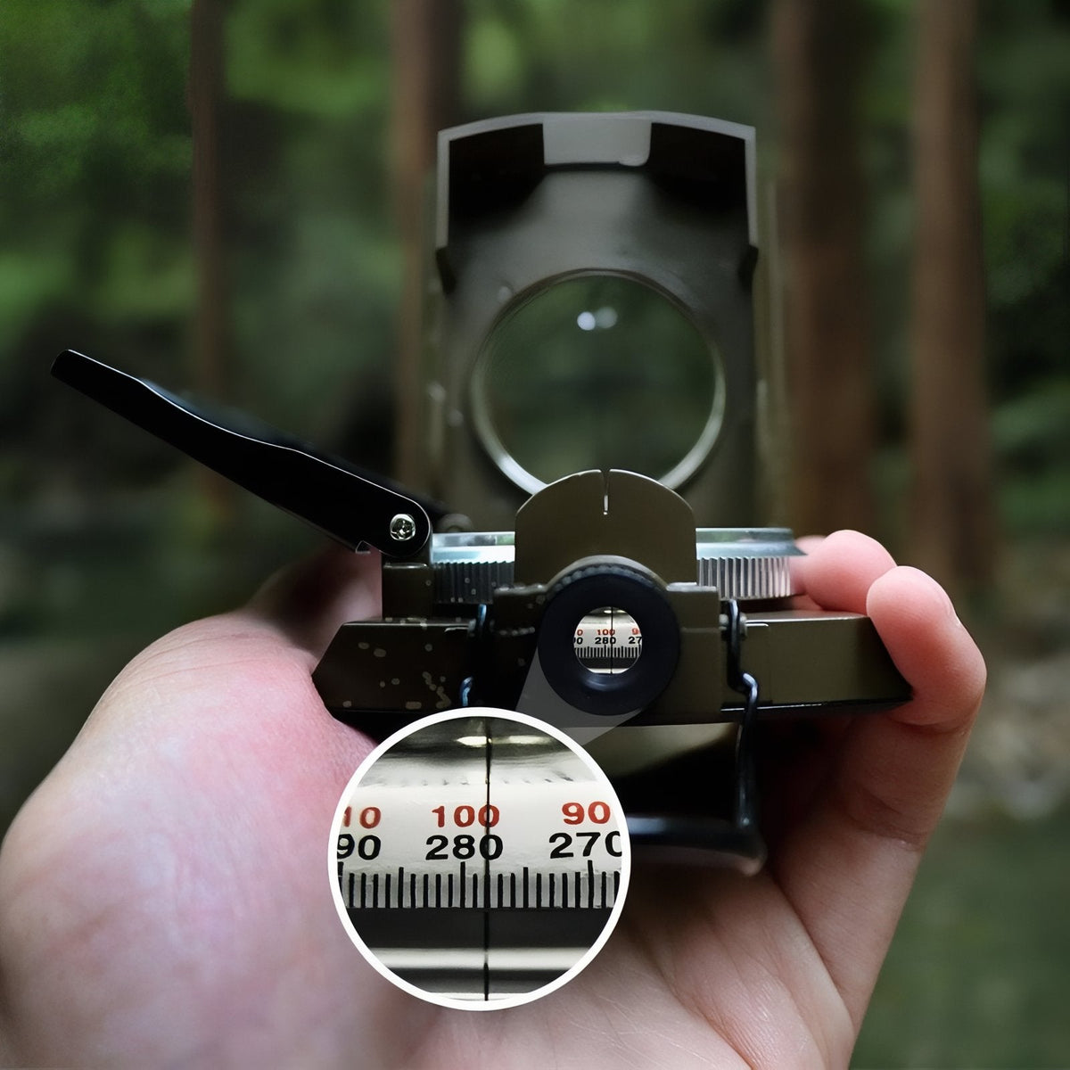 Hand holding the open sighting compass up to the eye in a forest, with an inset of the bearing scale seen through the lens