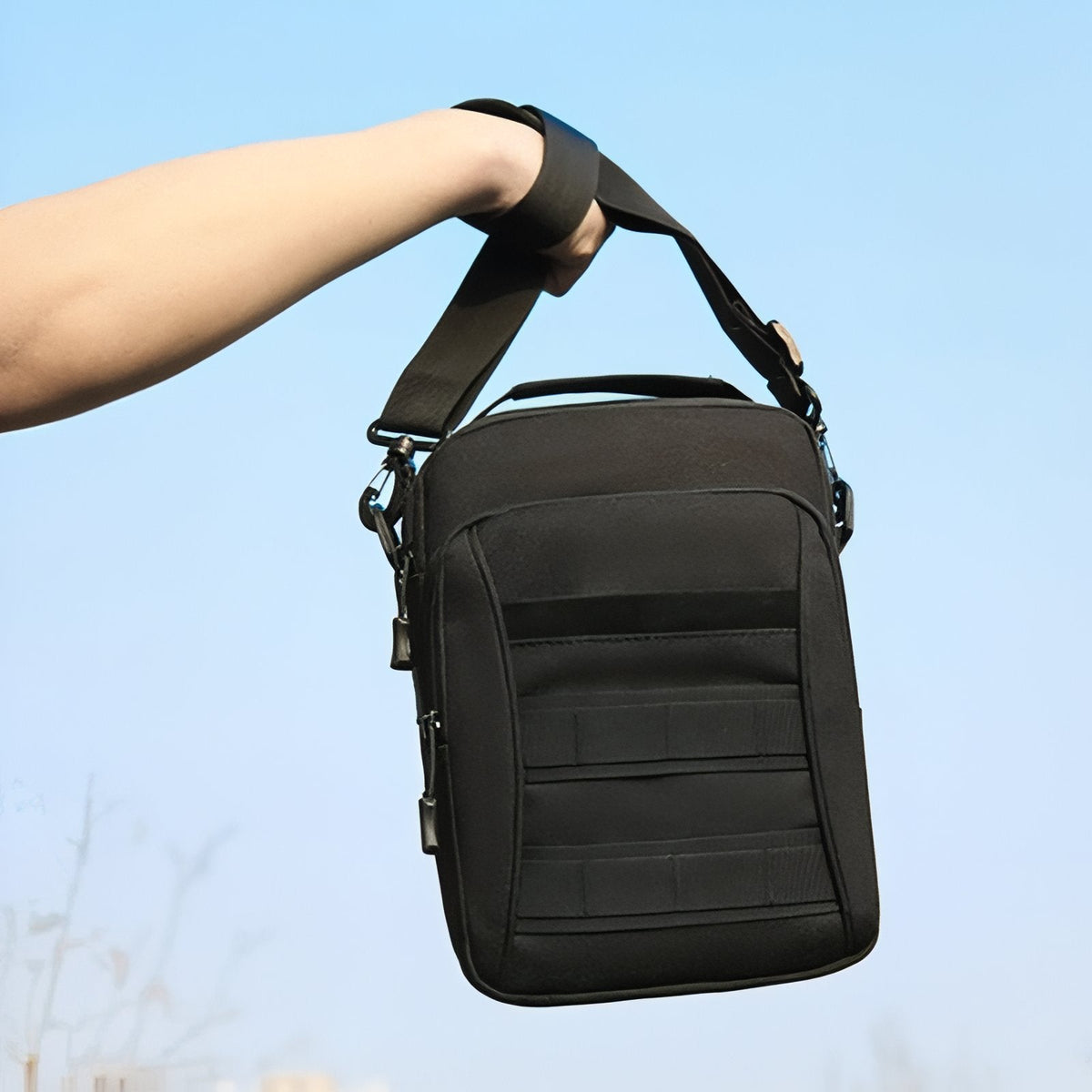 Black tactical shoulder bag held up by its shoulder strap against the sky