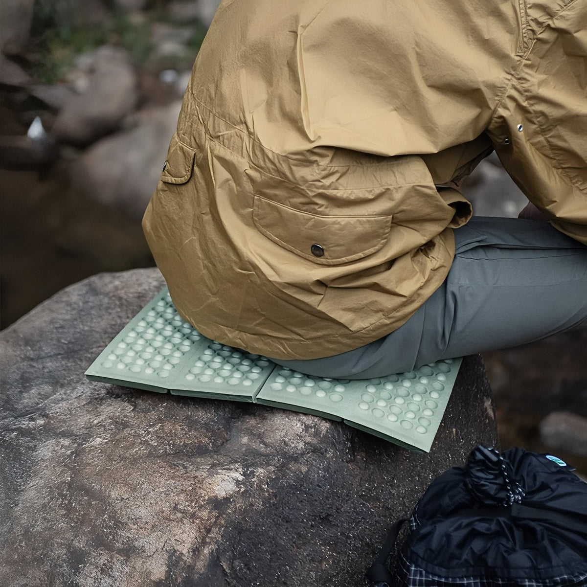 Close view of a hiker sitting on the green foam sit pad on a boulder, the pad bending over the rock's edge