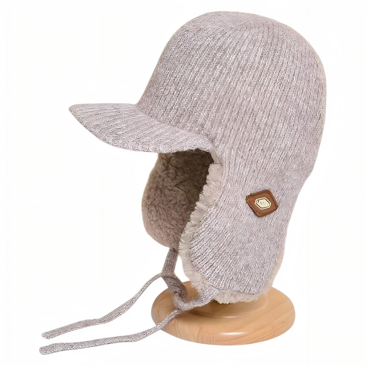 Beige knitted trapper hat with a short brim and plush-lined ear flaps on a wooden hat stand