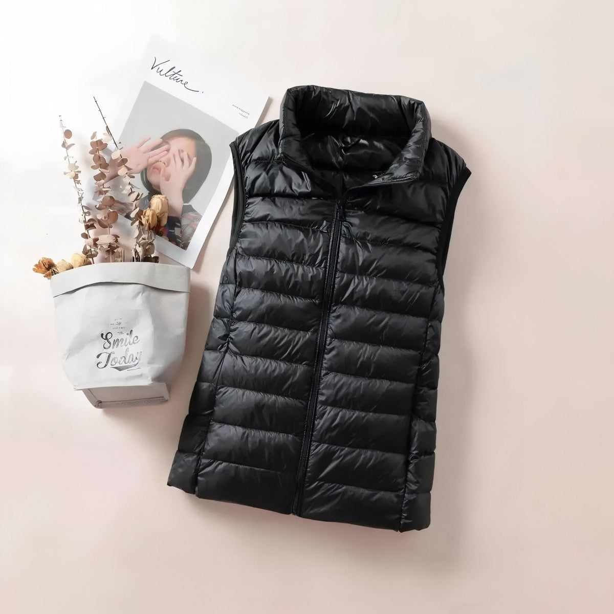 Black quilted vest laid flat beside a magazine and dried flowers
