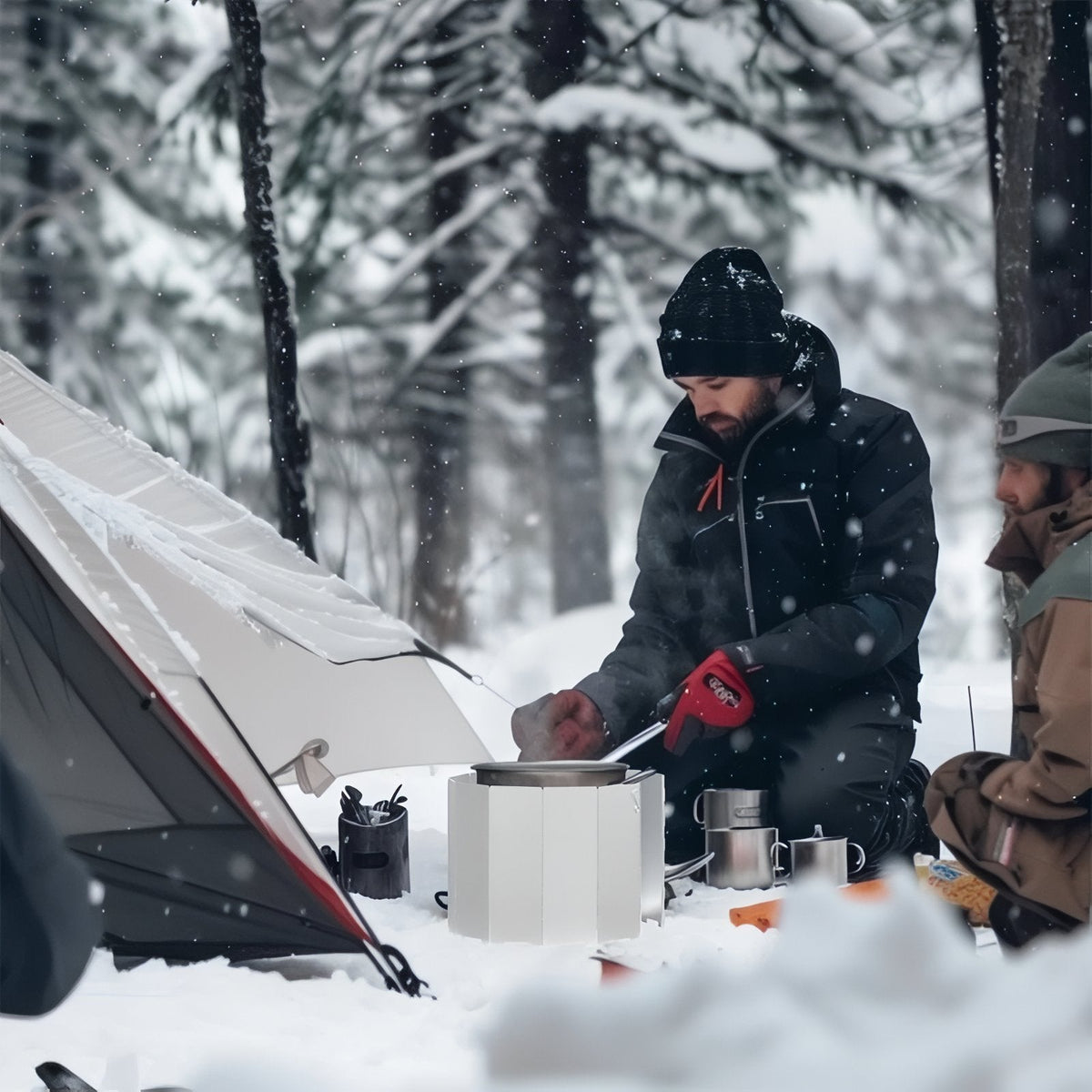 Two campers cooking in the snow behind the aluminium windscreen set round their stove