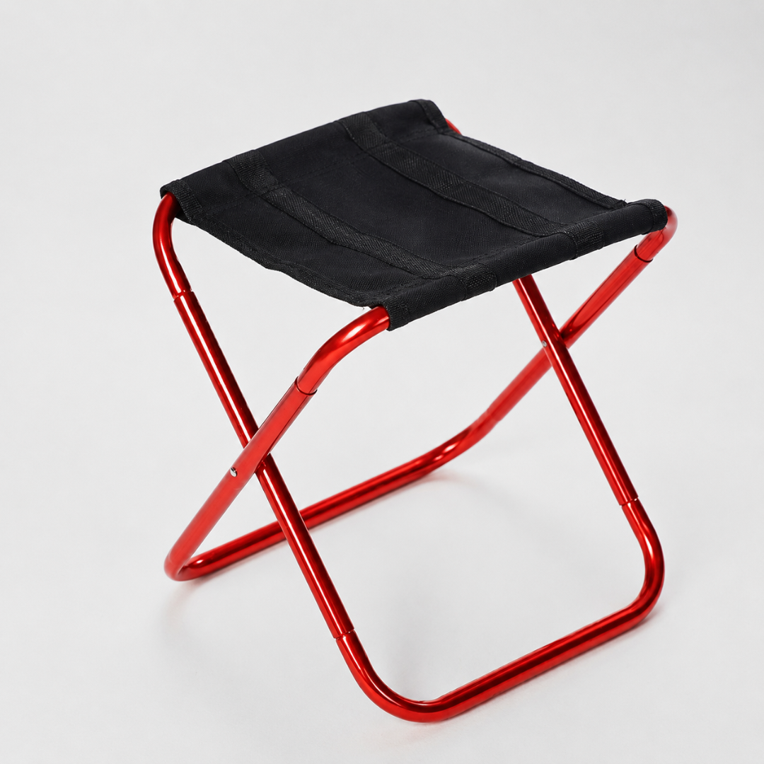 A folding stool with a bright red aluminium frame and a black canvas seat, photographed against a plain grey studio background.