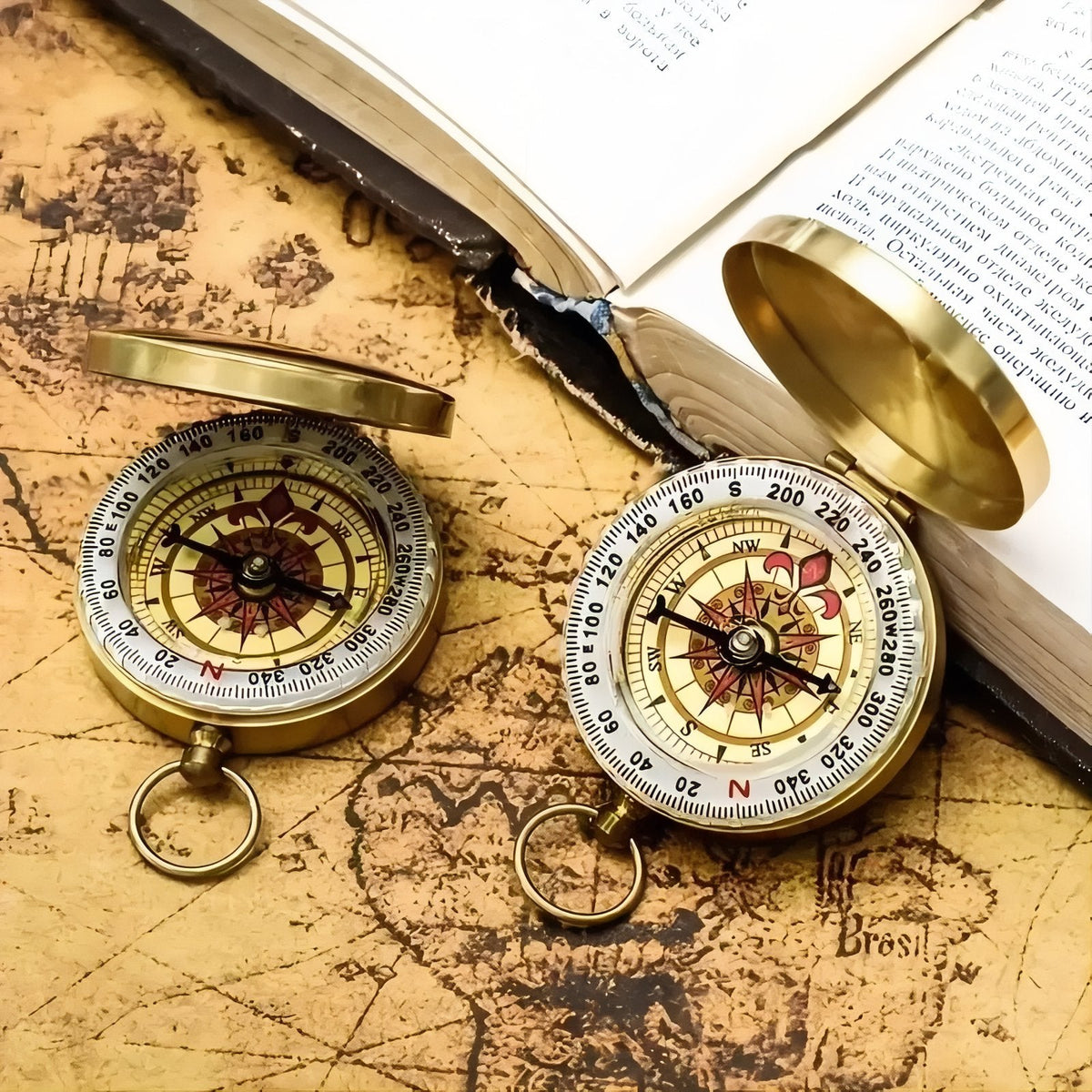 Two open pocket compasses on an old map beside an open book