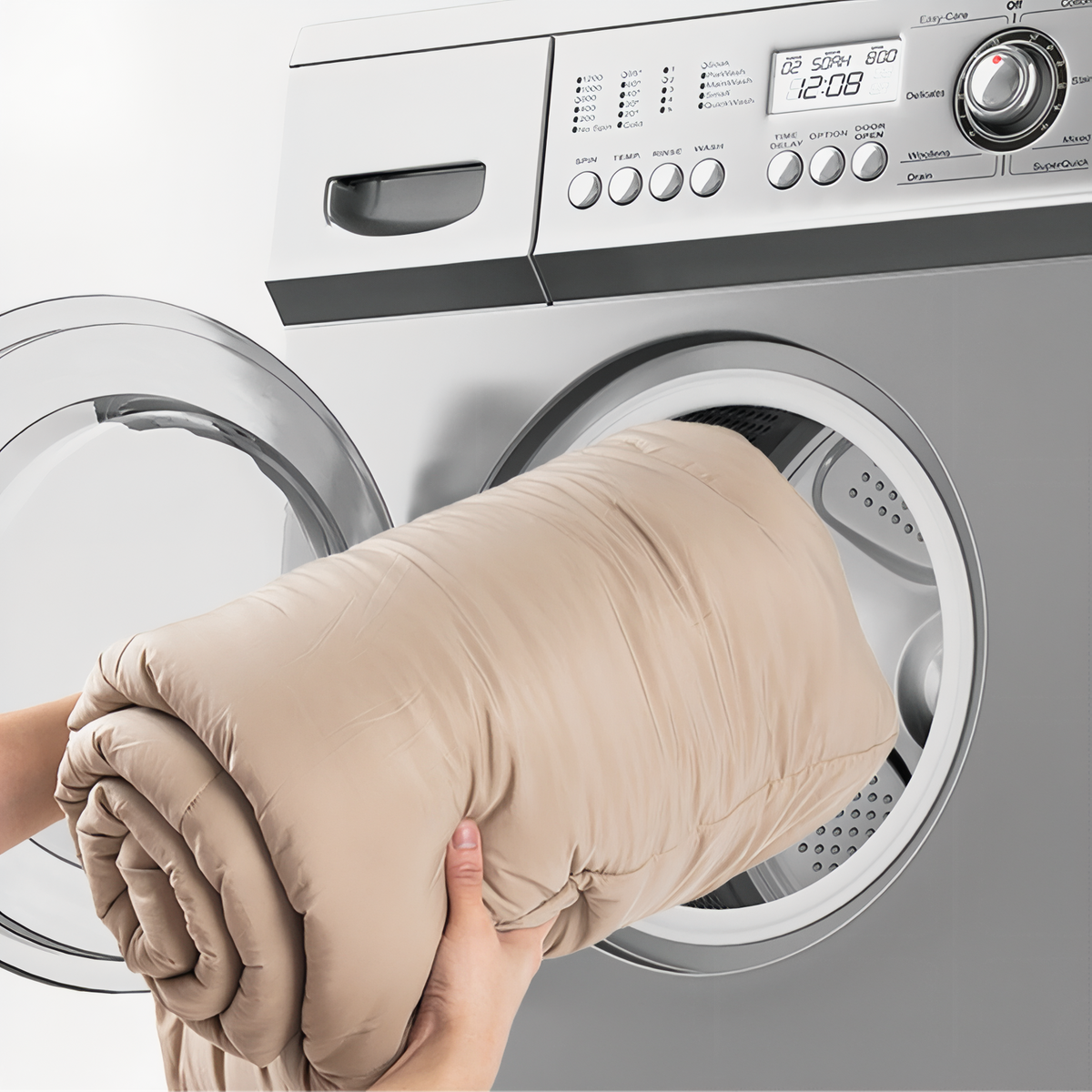 The rolled-up beige sleeping bag being pushed into the drum of a front-loading washing machine