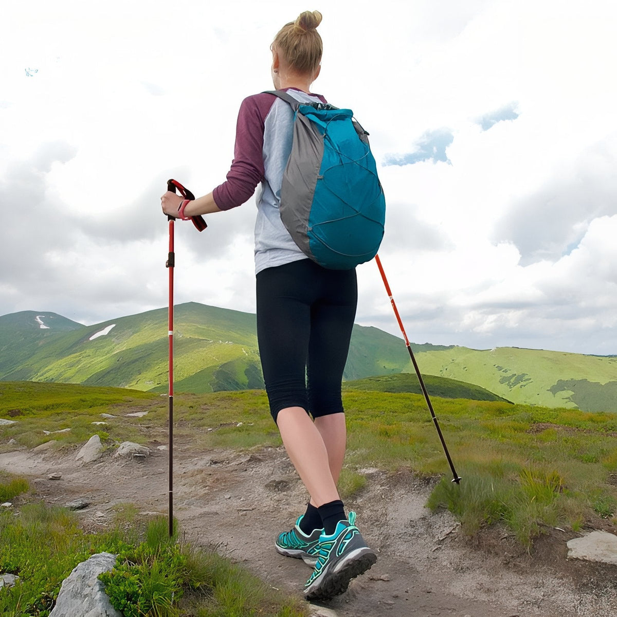 Hiker with a day pack walking a mountain path with two red trekking poles
