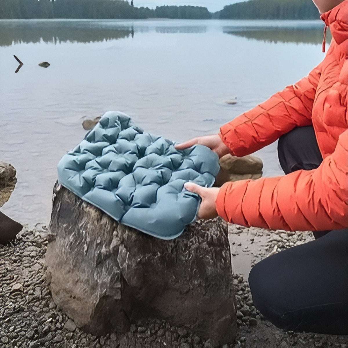 Hands placing an inflatable seat cushion on a rock by a lake