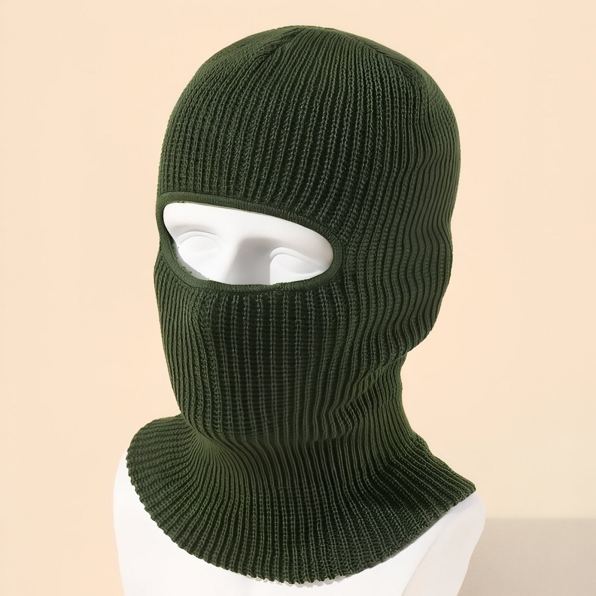 Olive green knit balaclava on a mannequin head against a peach background