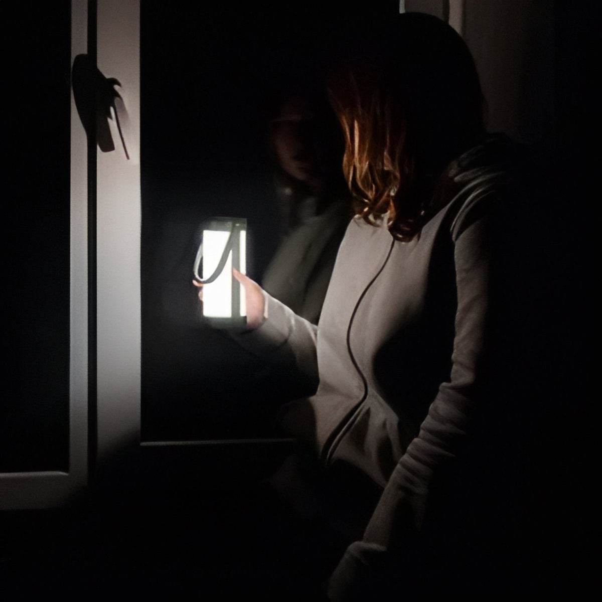 Person holding the lit lantern by its handle in a dark doorway