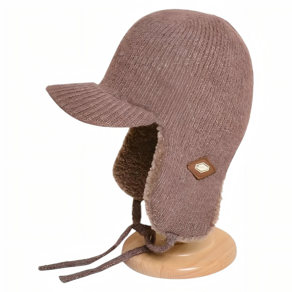 Light brown knitted trapper hat with plush ear flaps on a wooden hat stand