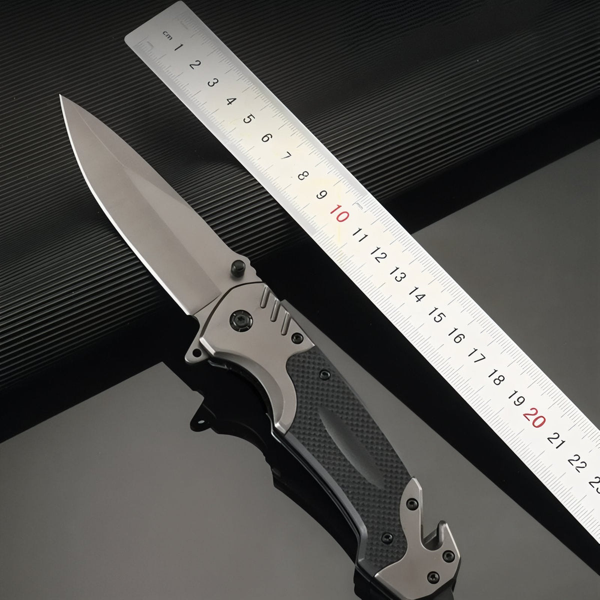 Open folding knife beside a steel ruler reading to about 23 cm
