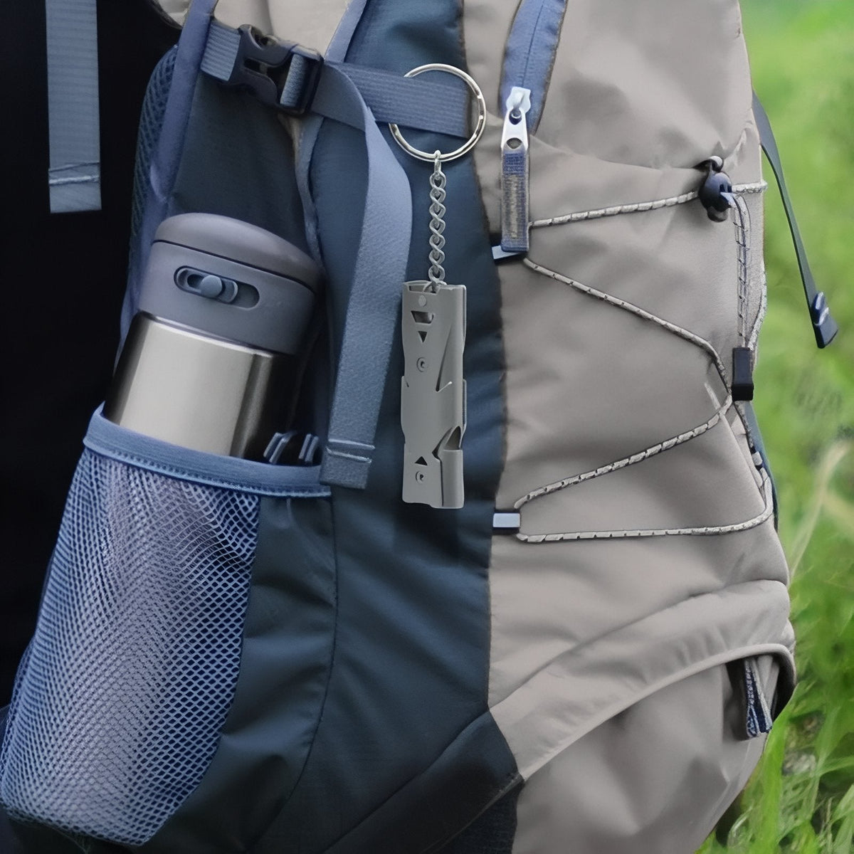 Silver grey whistle hanging from a backpack shoulder strap by its split ring