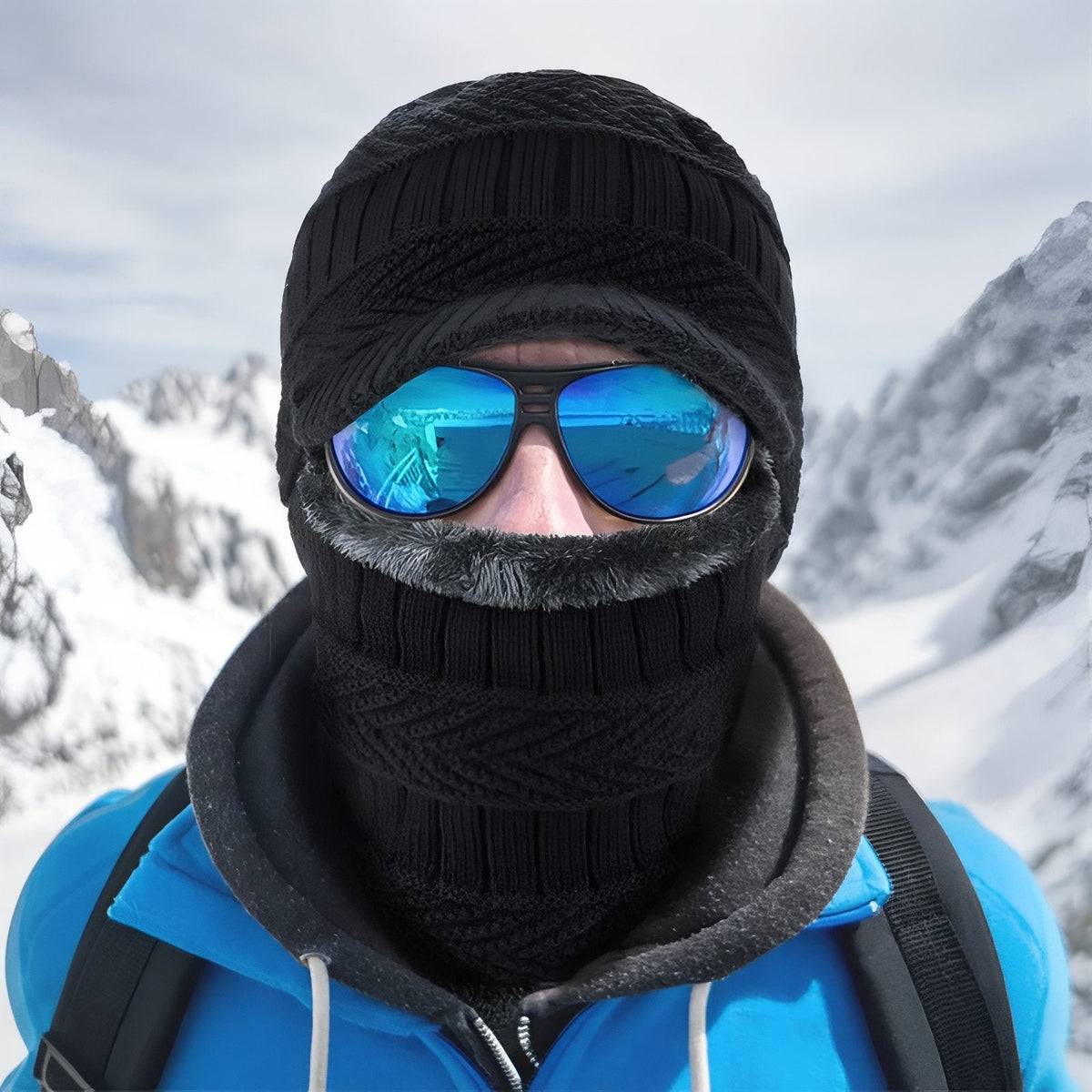 Hiker in the snowy mountains wearing the black knitted balaclava pulled up over the nose, with mirrored goggles
