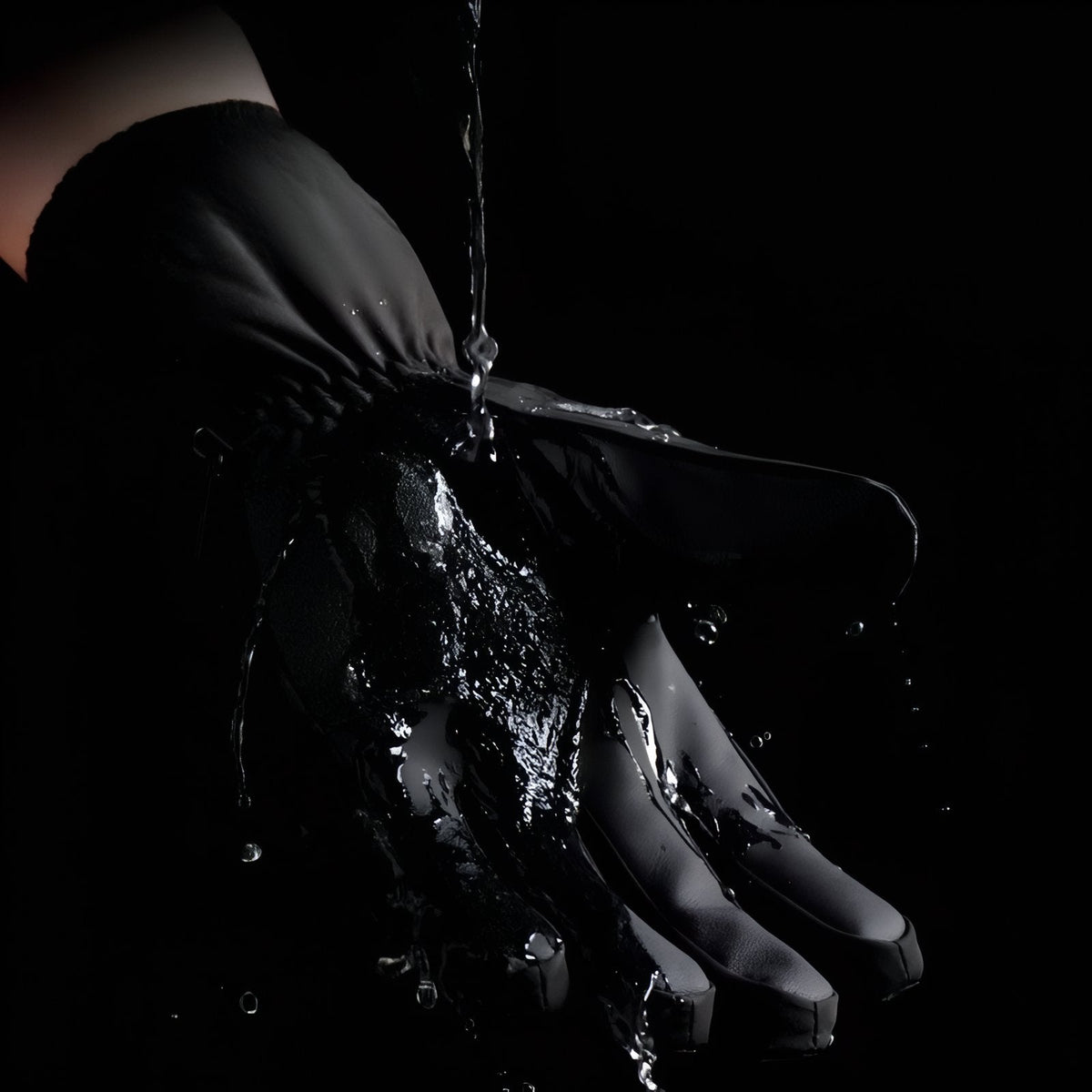 Water splashing over a black winter hiking glove against a dark background, beading off the shell