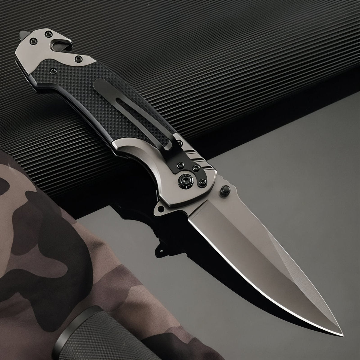 Open folding knife resting on a dark surface, pocket clip on the handle