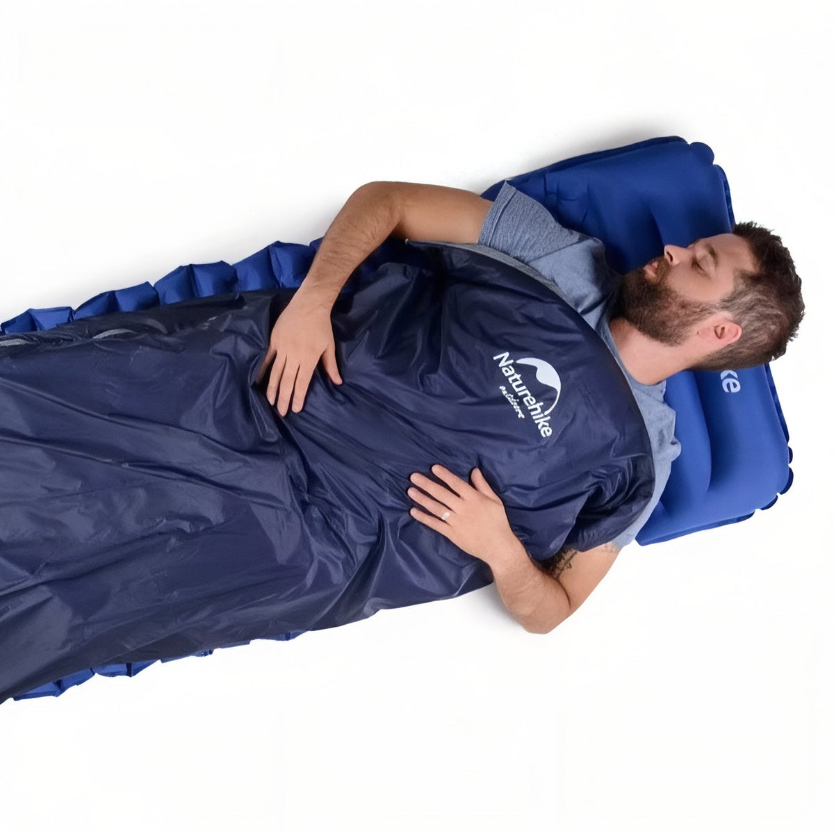 Man lying on his back in a navy envelope sleeping bag on an inflatable mat and pillow