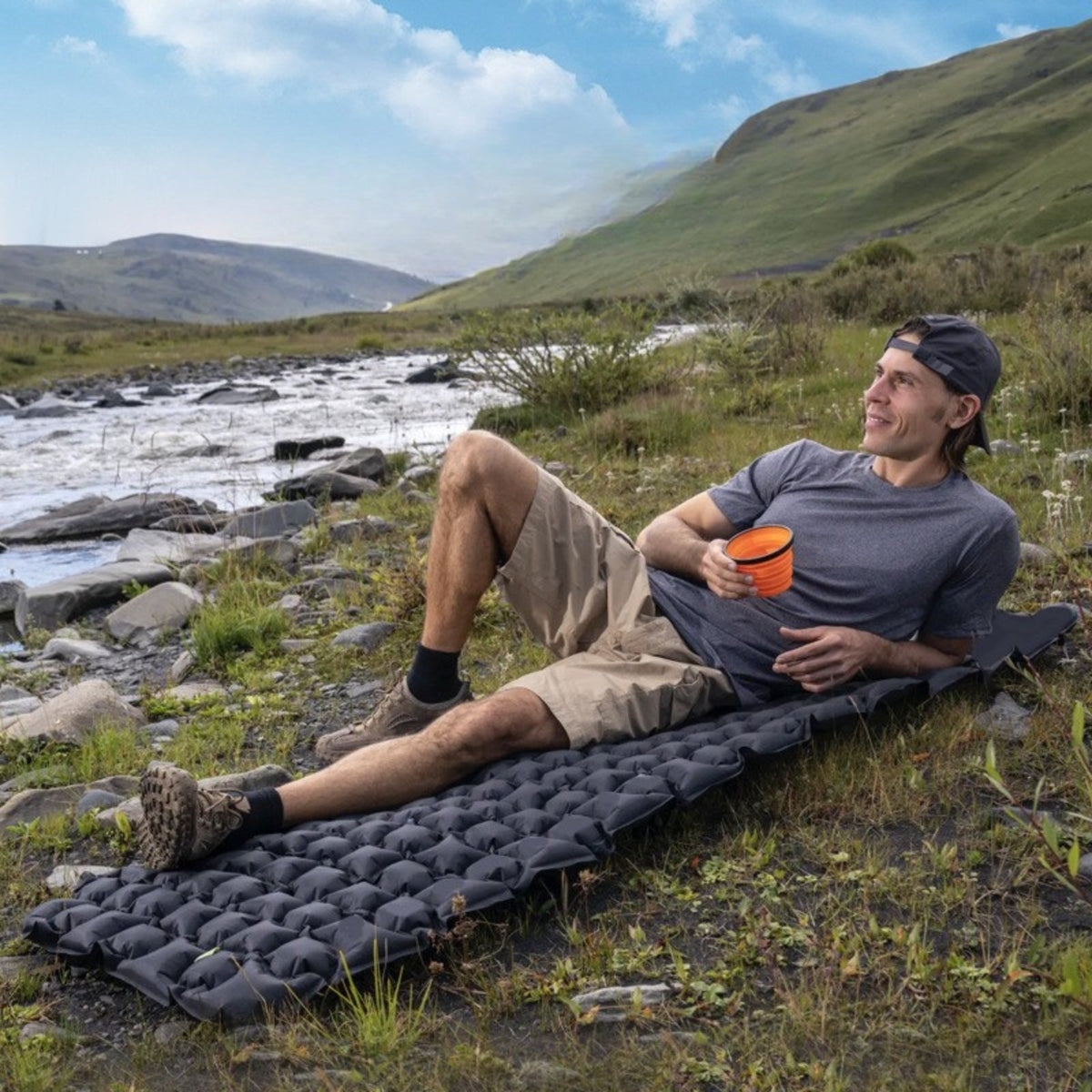 Man lying on the charcoal grey sleeping mat beside a mountain stream