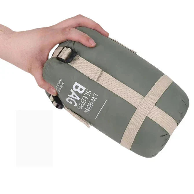 A grey-green sleeping bag packed into its printed carry sack with cream compression straps, held in one hand