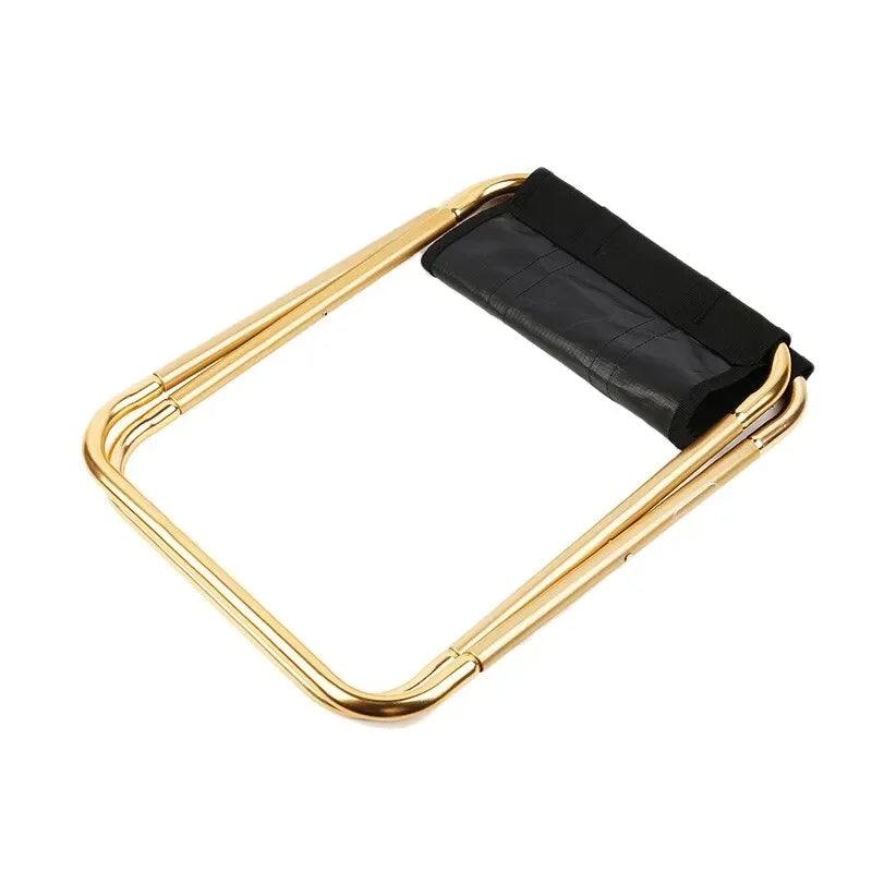 The gold stool folded flat and seen from above, with the black seat fabric gathered between the closed tubes.