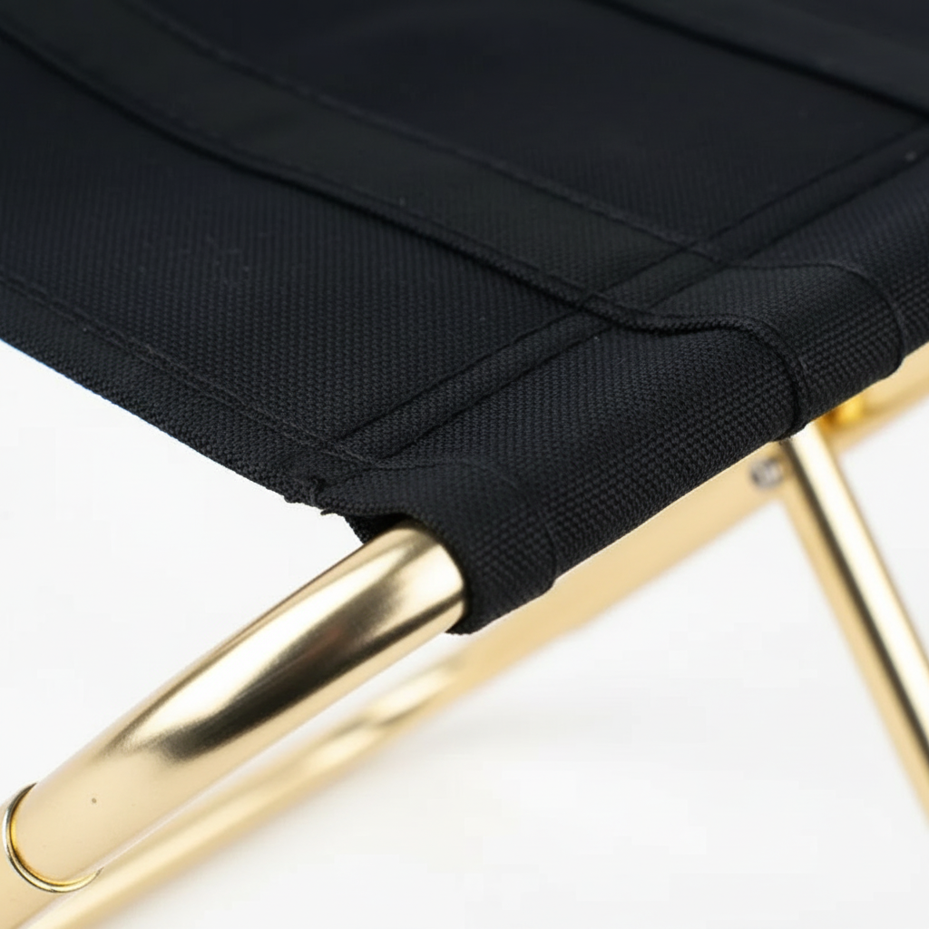 Close-up of the black woven seat fabric and its stitched seam where the cloth wraps over the gold tube frame.