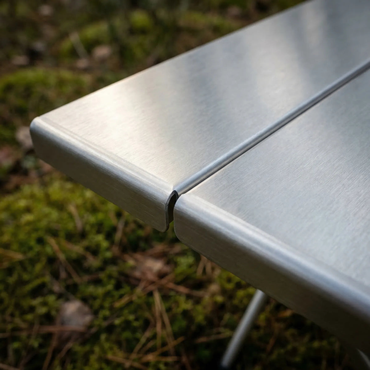 Close-up of the brushed stainless steel top, showing the rolled corner edge and the seam where the two panels meet.
