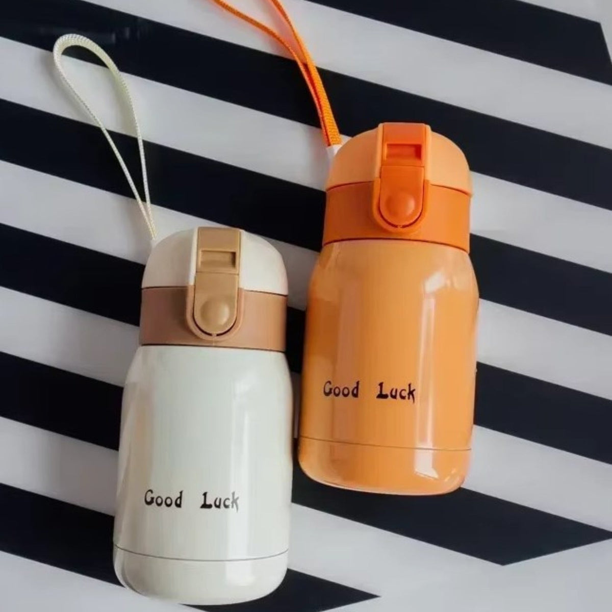 Cream and orange insulated bottles with their wrist straps on a striped cloth