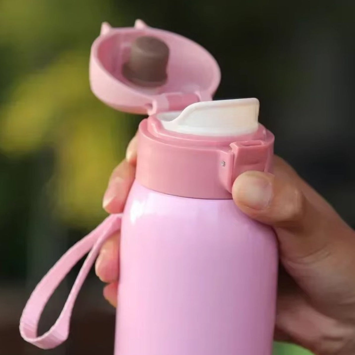 Pink bottle held in a hand with its lid flipped open to the spout and the wrist strap hanging