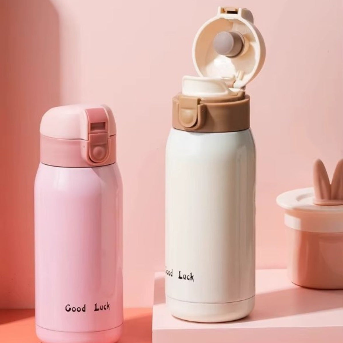 Pink and cream insulated bottles on a shelf, the cream one with its lid flipped open