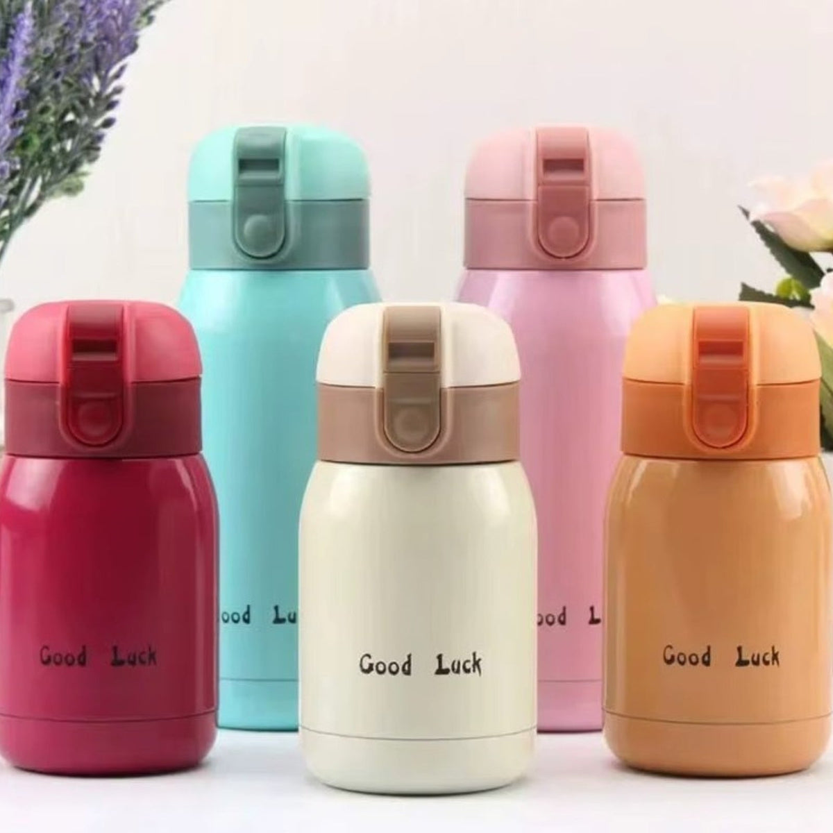 Five insulated bottles in raspberry, turquoise, cream, pink and orange, printed with the words Good Luck