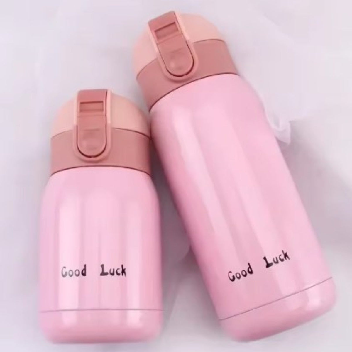 Two pink insulated bottles, 200 ml and 360 ml, lying on a soft cloth