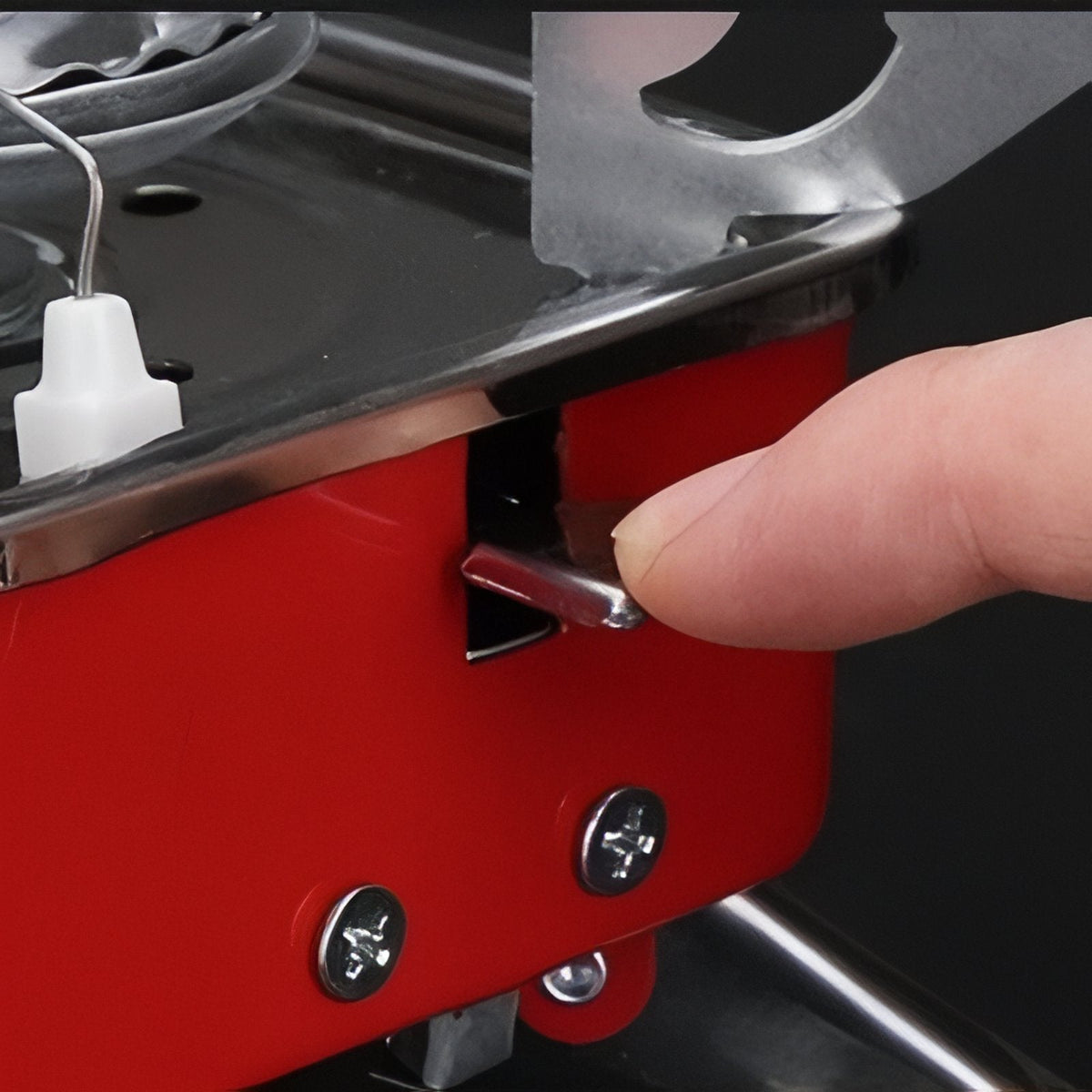 Finger pressing the piezo ignition lever on the front of the red stove