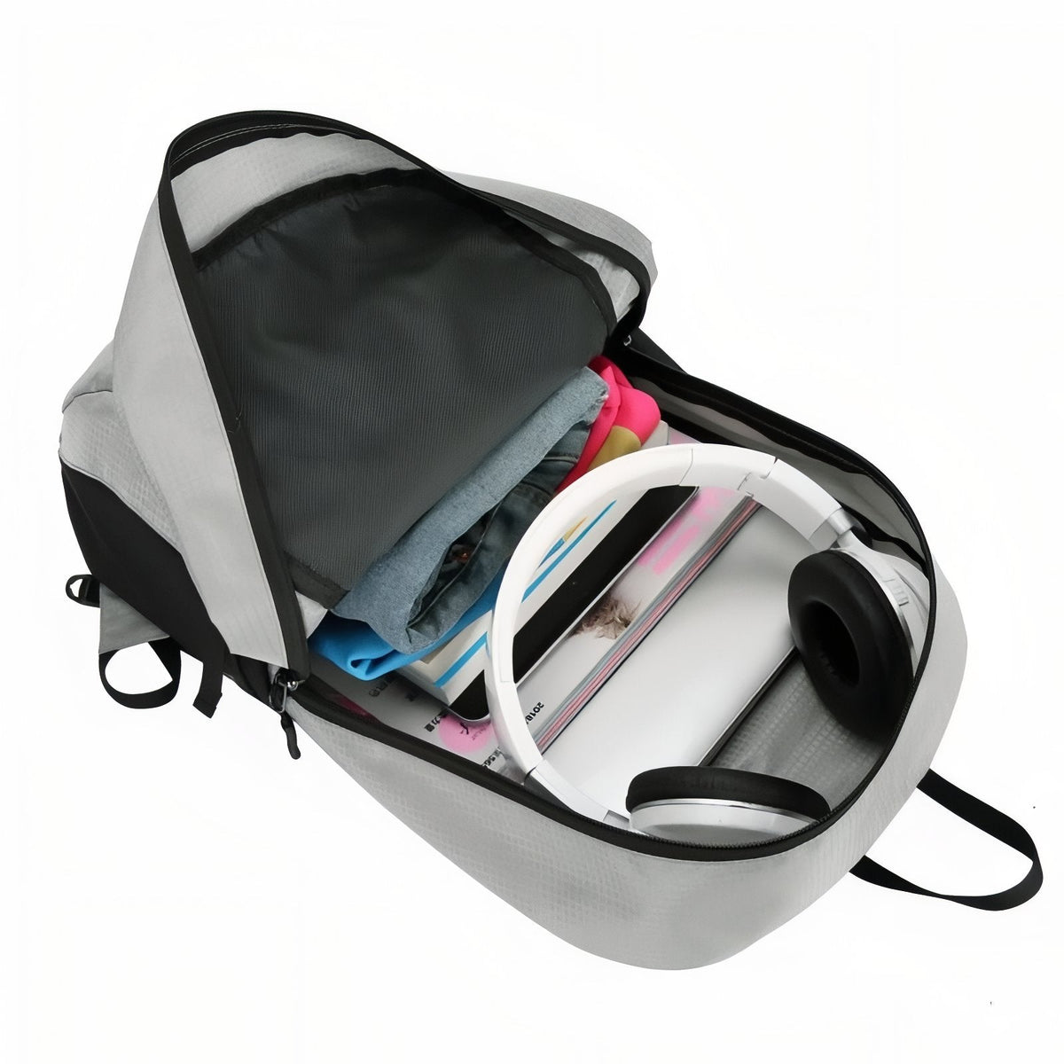 The light grey daypack unzipped, showing clothes, a book and headphones packed in the main compartment