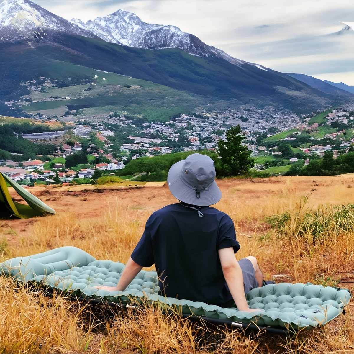 Man sitting on the sage green sleeping mat on dry grass with mountains behind